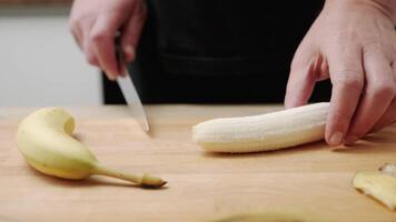 Close-up of hands slicing fresh banana on wooden cutting board in kitchen environment video