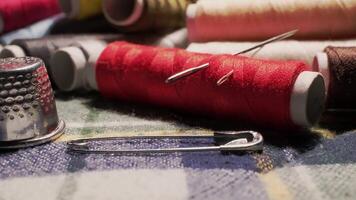 Close-up of Colorful Spools of Thread, Needles, Safety Pin and Metal Thimble on Fabric Surface in Sewing Workspace video