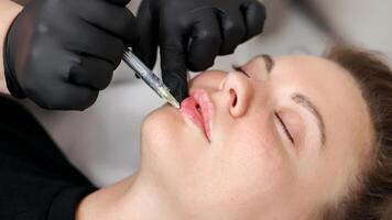 Hands of a specialist giving an injection into the lips of a young woman. Lip augmentation and correction procedure. photo