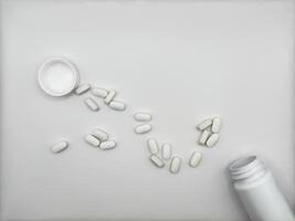 White pills for illness lie on white background spilled out of white medicine jar surface front view photo