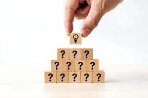 Hand places lightbulb block on pyramid of question mark blocks symbolizing idea generation photo