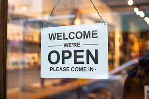 Welcome we re open please come in sign hanging on a storefront window photo