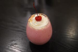 A pink milkshake with whipped cream and a cherry on top photo