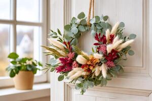 Beautiful autumnal wreath hanging on a white door with eucalyptus leaves, bunny tails grass, and colorful flowers photo