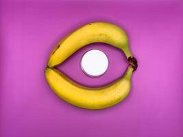 Two bright yellow bananas create a circle in which lies a jar with a white lid for medicines, top view, in the center of the image photo