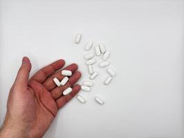 White pills for illness fell out of a man's hand in a pile on a white background, hand on the left in the image top view photo