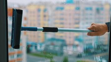 Washing a window in the city. Wet window is cleaning with special brush on blur background of multi-storey buildings. video