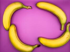 Background of four bright yellow bananas lying on the side of the image on a purple background, top view photo