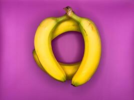 Jenga game of four bright yellow bananas lying on purple background, top view, center of image photo