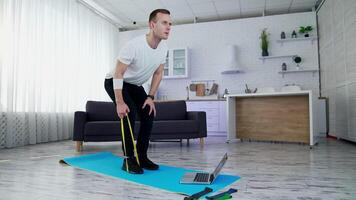 Concentrated man exercising with a rubber band at home. Young man doing working out while standing on a mat in the kitchen. Sportive lifestyle during quarantine. video