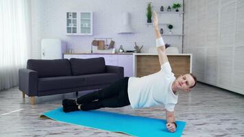 Young man is training at home. Man doing exercise on a mat on kitchen background. Guy working hard to maintain body shape during isolation. video