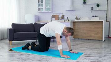 Guy doing his workout at home. Young man on a mat doing exercise of flexion and extension his back on kitchen background. Training during lockdown. video