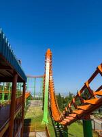 Orange roller coaster at an amusement park with cloudy blue sky, vertical photo for social media, copy space