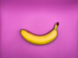 One bright yellow banana lies horizontally on a purple background, top view, centered in the image photo