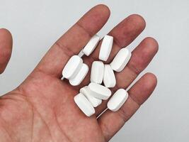 White pills for illness lie in a man's hand on a white background, hand on the left in the image top view photo