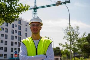 Professional male construction worker with safety helmet and reflective vest smiling confidently at a construction site with building progress in the background photo