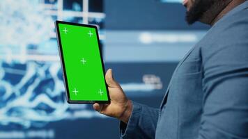 Black IT specialist examining algorithmic data next to chroma key, using tablet in a high tech environment with futuristic digital visuals. AI smart technology and neural networks. Camera B. video