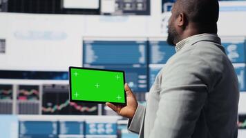 Black businessman holding device with green screen and examining dashboards, ensuring business productivity for achievement in economy industry. Performance metrics and insight. Camera B. video
