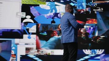 Black presenter hosting conference on stage surrounded by media visuals, symbolizing global convention with live audience to discuss about online trends and mobile apps. Public event. Camera A. video