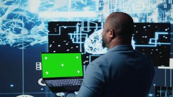Black male engineer showing laptop with chroma key display next to predictive analytics immersed in AI brain development and deep learning. High tech cybernetics algorithms. Camera A. video