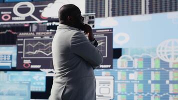 African american entrepreneur contemplating about a new strategy to increase the company profit while he evaluates infographics and fintech insight with digital tools. Leadership. Camera B. video