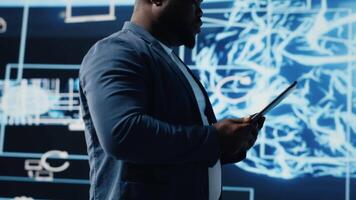 African american IT specialist ensuring futuristic AI brain in the background, machine learning through neural networks and cloud computing platforms. Algorithmic thinking. Camera B. video