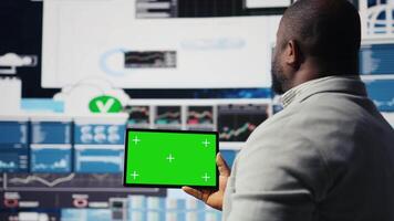Black businessman holding device with green screen and examining dashboards, ensuring business productivity for achievement in economy industry. Performance metrics and insight. Camera A. video
