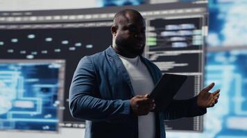 African American developer working on programming and automation, coding on a laptop with a futuristic interface behind him. Tech professional thrives in a world of AI and code snippets. Camera B. video
