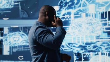 noir technologie spécialiste parlant sur téléphone intelligent appel dans un ai alimenté environnement, représentant prédictif algorithmes et machine apprentissage systèmes. travail sur automatisation et innovation. caméra b. video