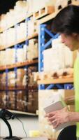 Vertical Asian depot worker in hi vis vest scanning barcode labels on boxes, retail operations in industrial fulfillment center. Male staff engages in AWB registration activity for delivery. Camera A. video