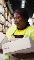 Vertical African american woman reviewing cargo labels for order processing, verifying the accuracy of shipping labels and details. Working for large business e-commerce warehouse operations. Camera A. video
