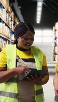 Vertical Diverse staff members using tablet for order processing and fulfillment, working on packing goods in warehouse space and ensuring easy import export products distribution. Camera A. video