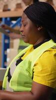 Vertical African american female worker typing awb shipment details on computer, updating package tracking software for clients. Person managing order fulfillment in a retail warehouse facility. Camera B. video