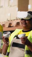 Vertical Black female employee with virtual reality glasses handling orders fulfillment via 3D simulation, parcel status on package tracking software. Artificial intelligence inventory control. Camera B. video