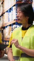 Vertical Multiethnic team in hi vis vests managing retail business operations, doing product handling from the warehouse big racks. Colleagues overseeing import export activity. Camera B. video