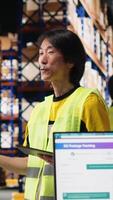 Vertical Asian worker promoting the large business industrial warehouse in a vlog, live streaming a for e-commerce shipment advertisement. Staff presenting the storage on commercial ad. Camera B. video