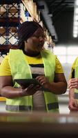 Vertical African american and asian team prepare shipments for dispatch with digital inventory and cargo pallets on depot racks. Working in a large scale distribution hub for express delivery. Camera A. video
