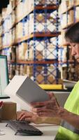 Vertical Worker verifying cardboard boxes and awb tags for parcel tracking, handling order processing before distribution. Man in hi vis vest working in e-commerce warehouse with industrial racks. Camera A. video