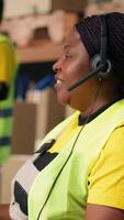 Vertical Black female customer support clerk speaks with clients about shipment details, helping with wrong address mix up on the help line. Woman resolves order, confirm airway bill numbers. Camera B. video