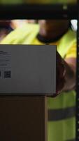Vertical Fulfillment center staff engages in airway bills scanning for order tracking, using scanner on shipping labels in the warehouse. Worker wearing hi vis vest in storage room with shelves. Camera A. video