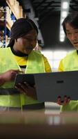 Vertical Black and asian workers managing the order fulfillment process in shipping area of a large business storehouse, racks filled with packages. Staff oversees parcel distribution operations. Camera A. video