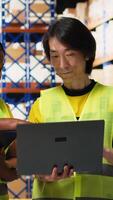 Vertical Black and asian workers managing the order fulfillment process in shipping area of a large business storehouse, racks filled with packages. Staff oversees parcel distribution operations. Camera B. video