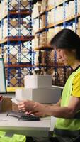 Vertical Man in hi vis vest reviews shipment details on awb tags for dispatch in industrial warehouse, parcels from the storage racks with tracking numbers for seamless express delivery. Camera A. video