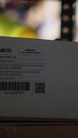 Vertical Fulfillment center staff engages in airway bills scanning for order tracking, using scanner on shipping labels in the warehouse. Worker wearing hi vis vest in storage room with shelves. Camera B. video