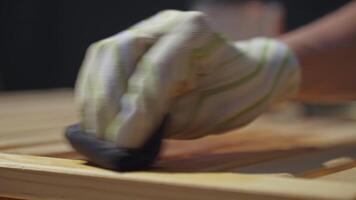 Gloved hand applying wood oil to a wooden bench, with a visible contrast between oiled and untreated areas video
