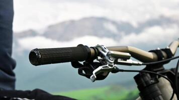Mountain MTB bike handlebars against the backdrop of epic mountains in the clouds in defocus. Male rider puts his hand on the bicycle handlebar video