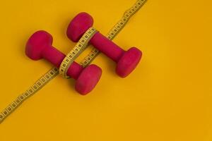 Concept of healthy lifestyle, weight loss, diet. Pink dumbbells for sports and yellow tape measure on yellow background with space for text. photo