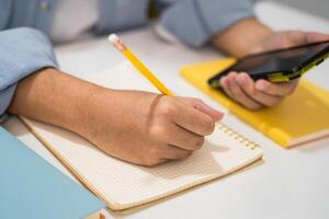Teenage write notebook and use mobile phone search data online to online learning education. photo