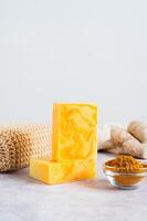 Bars of homemade turmeric soap and powder in bowl on table vertical view photo