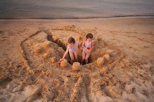 Sisters building a grand sandcastle at sunset on the beach photo